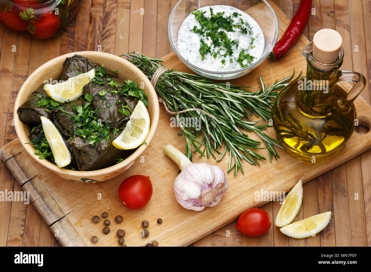 Dolma servita con fettine di limone, il coriandolo, panna acida Salsa con aglio su una tavola di legno. Olio di oliva con rosmarino. Foto Stock