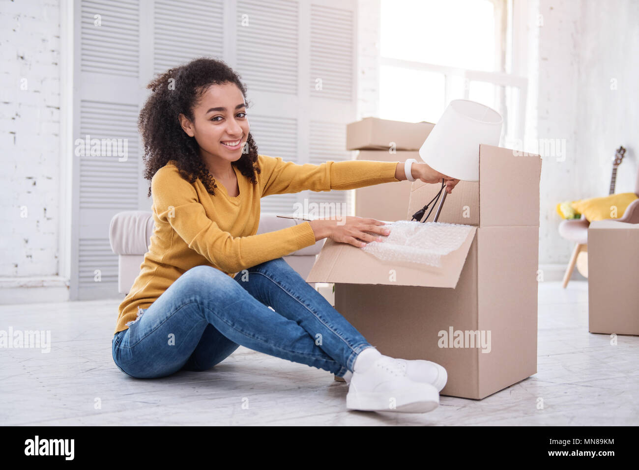 Affascinante curly-ragazza dai capelli in posa mentre imballo lampada da tavolo Foto Stock