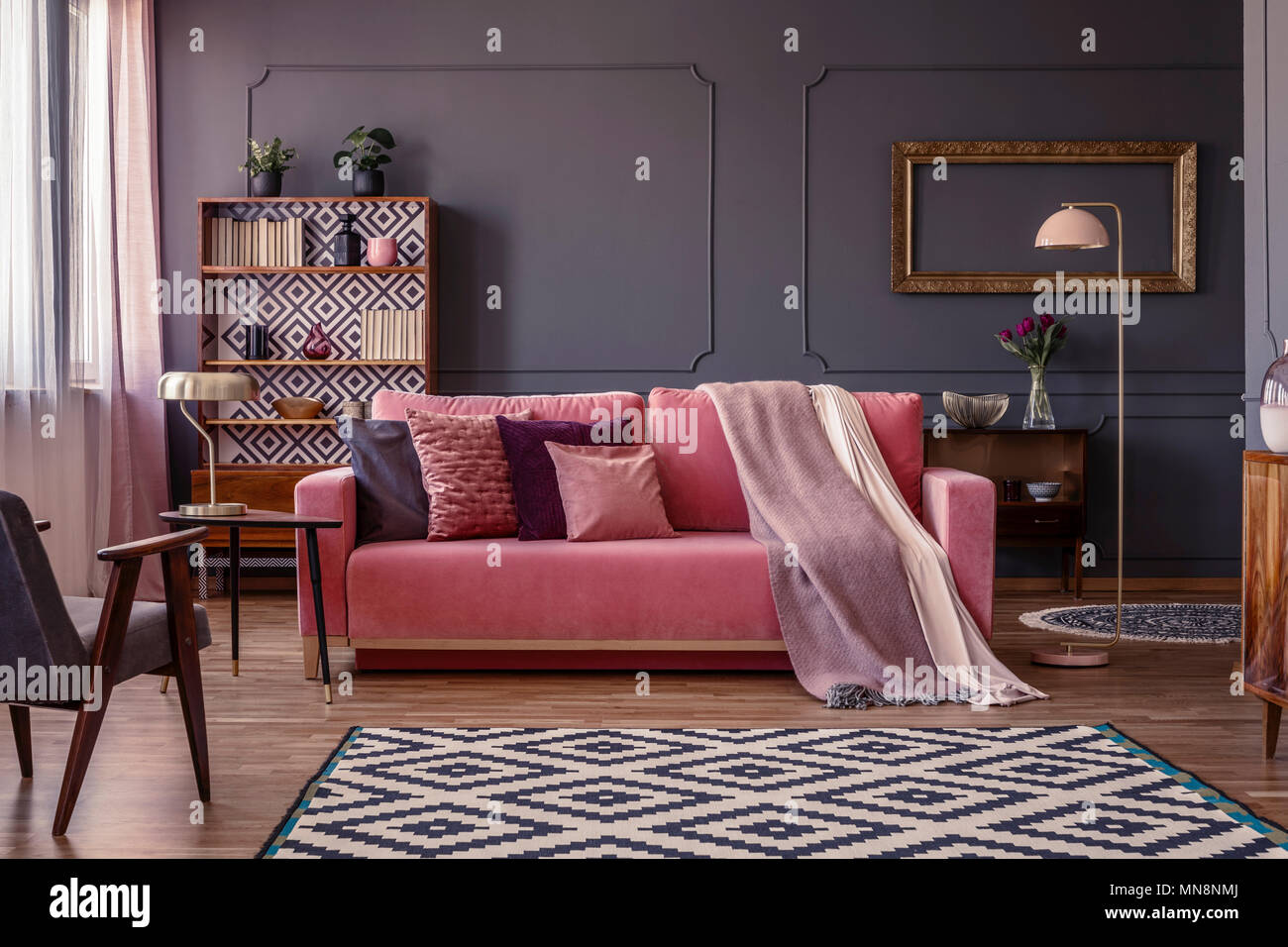 Rosa pastello coperta su un abbinamento divano nel soggiorno interno con elegante cornice dorata al buio su un muro grigio Foto Stock