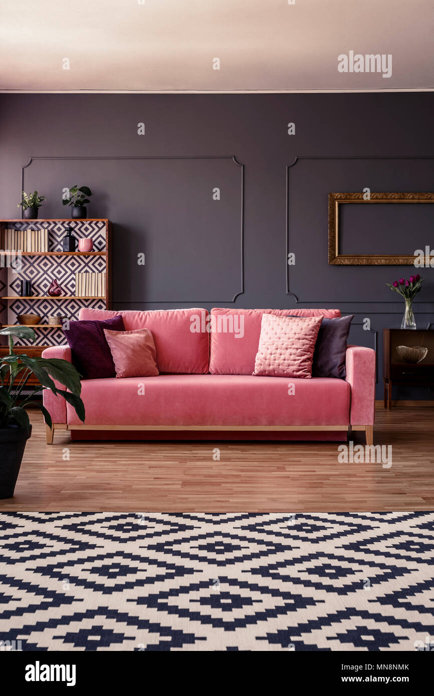 In velluto rosa lettino con cuscini in piedi nel centro di grigio scuro soggiorno interno con stampaggio sulla parete e tappeto geometrico Foto Stock