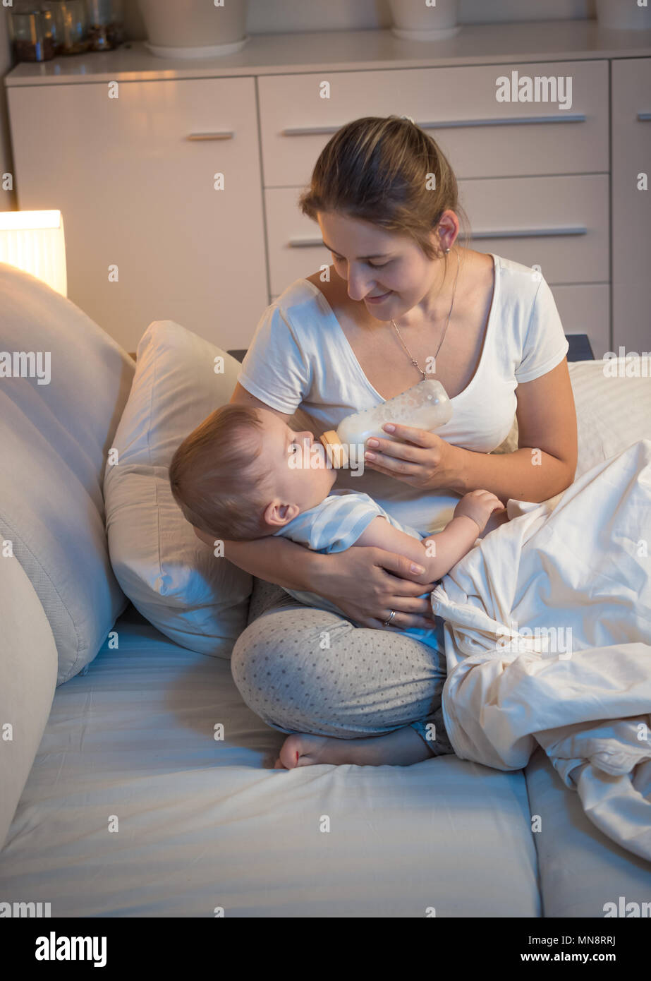 Giovane madre dando una bottiglia di latte per il suo bambino affamato di notte Foto Stock