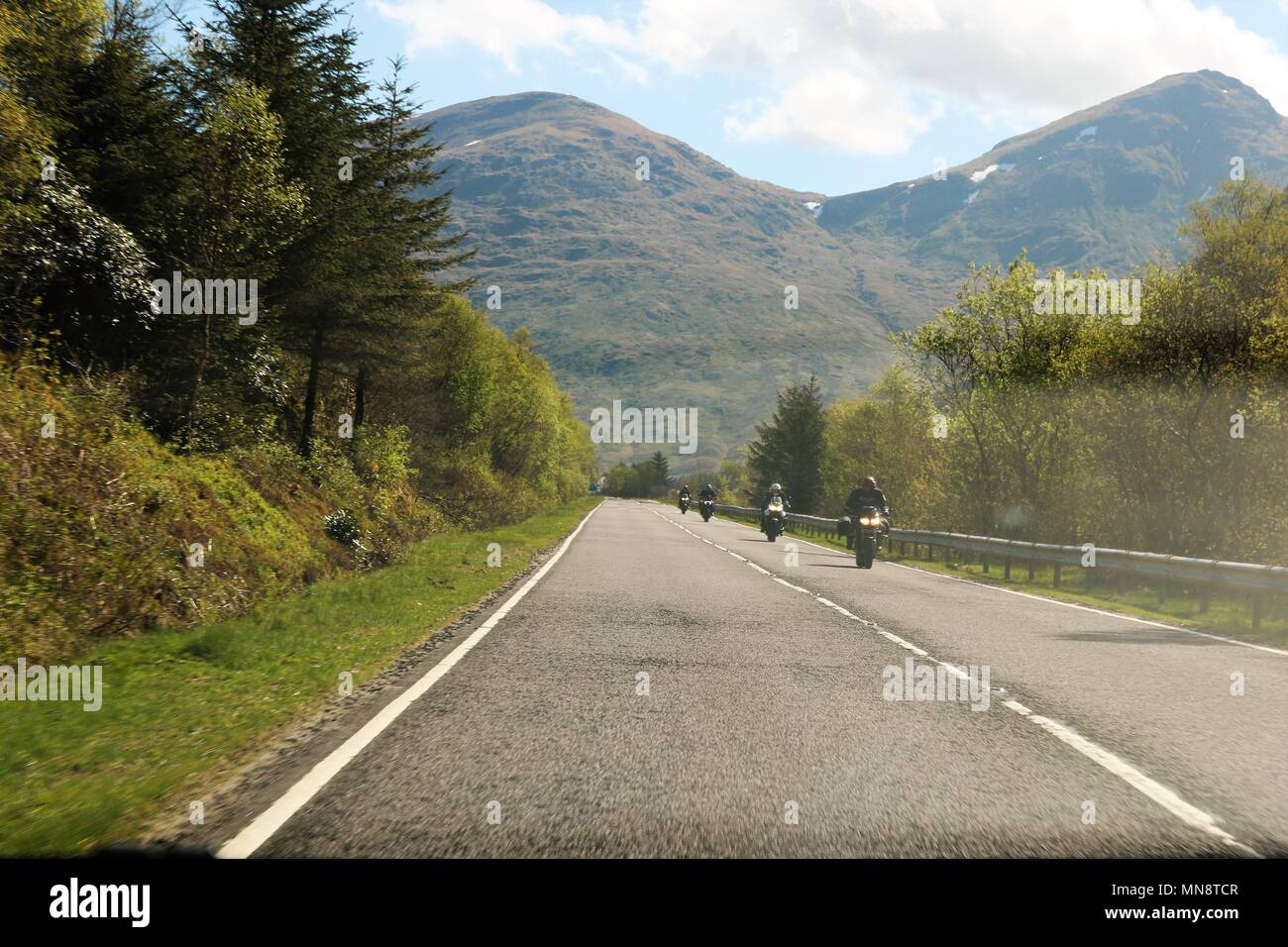 Motociclisti su strada intorno alla bellissima Loch Long, Scozia in una limpida giornata di sole che mostra acqua e montagne in una vista mozzafiato. Foto Stock