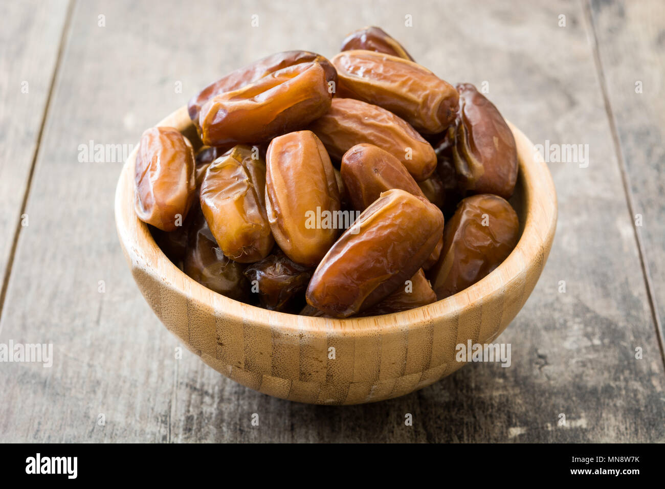 Date in ciotola di legno su sfondo di legno Foto Stock