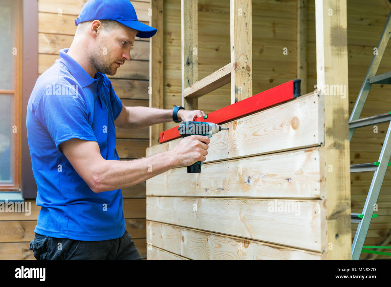 Costruzione capannone - lavoratore installazione facciata in legno tavole Foto Stock