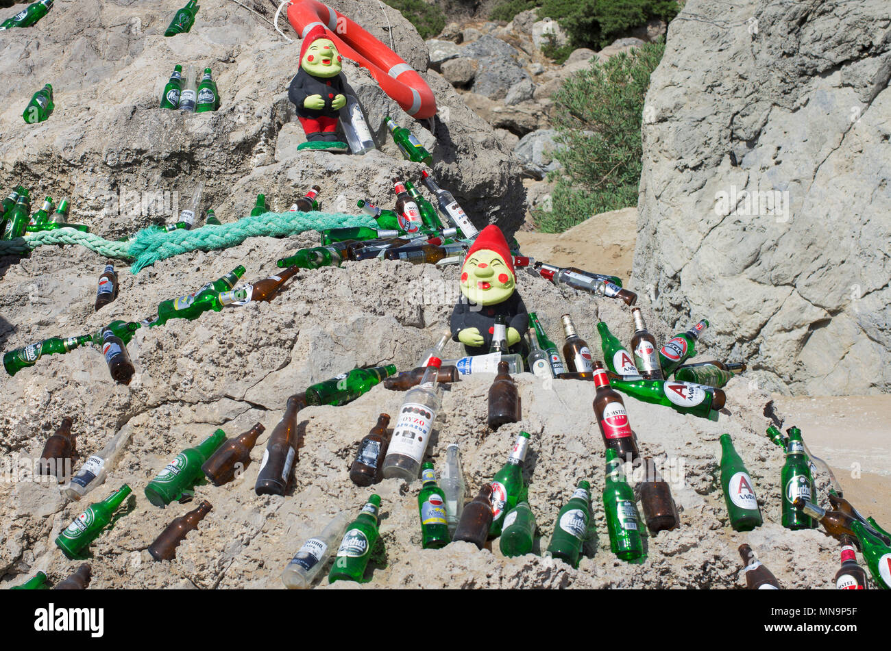 La spiaggia di Tsampika, l' isola di Rodi, Grecia - 21 Settembre 2017: due figure di gnomi tra splendidamente esposte le bottiglie da birra vuote su un enorme bould Foto Stock