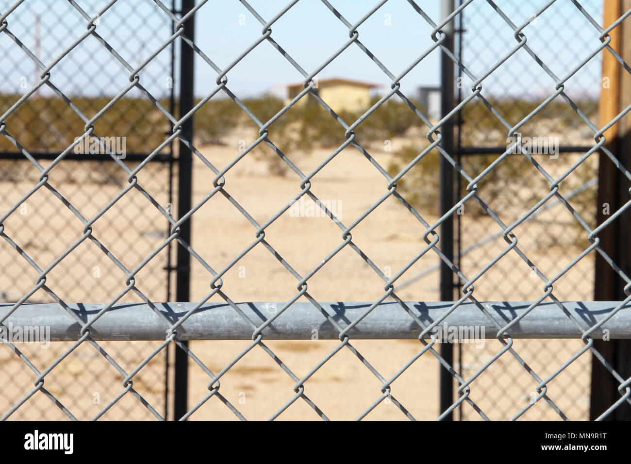 Un lontano abbandonato homestead attraverso una catena collegamento recinto, forte di una prigione vibe, Wonder Valley in California's High Desert, il Mojave, negli Stati Uniti. Foto Stock