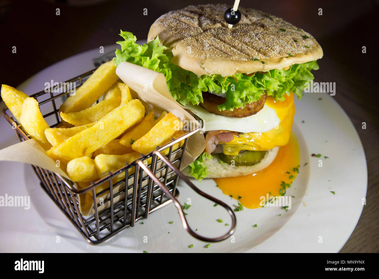 Un burger e servito con patate fritte. Il Burger dispone di un anello di cipolla, uova fritte e insalata. Foto Stock