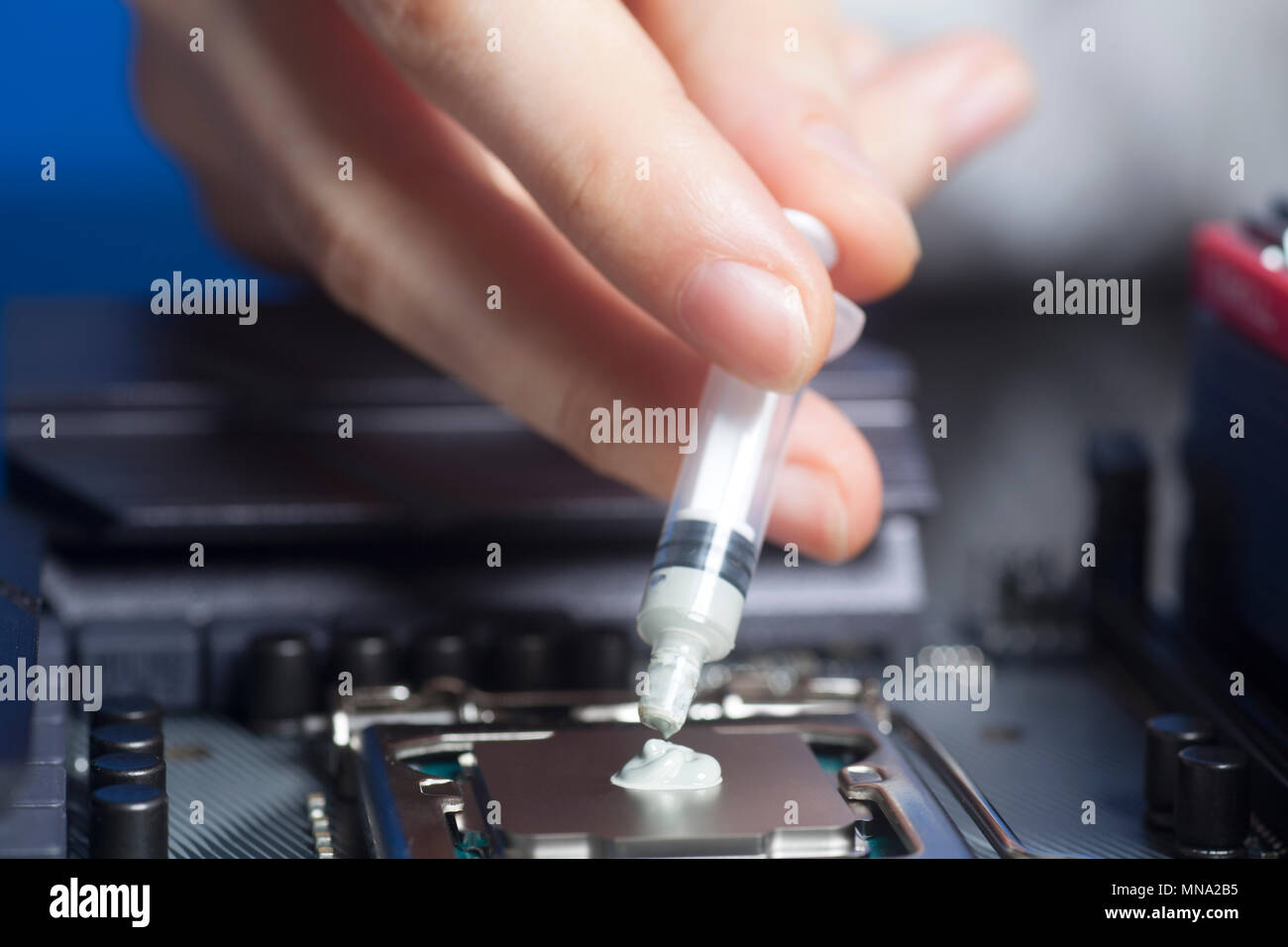 Mano con una siringa di applicare la pasta termica sul processore CPU su scheda madre Close up Foto Stock