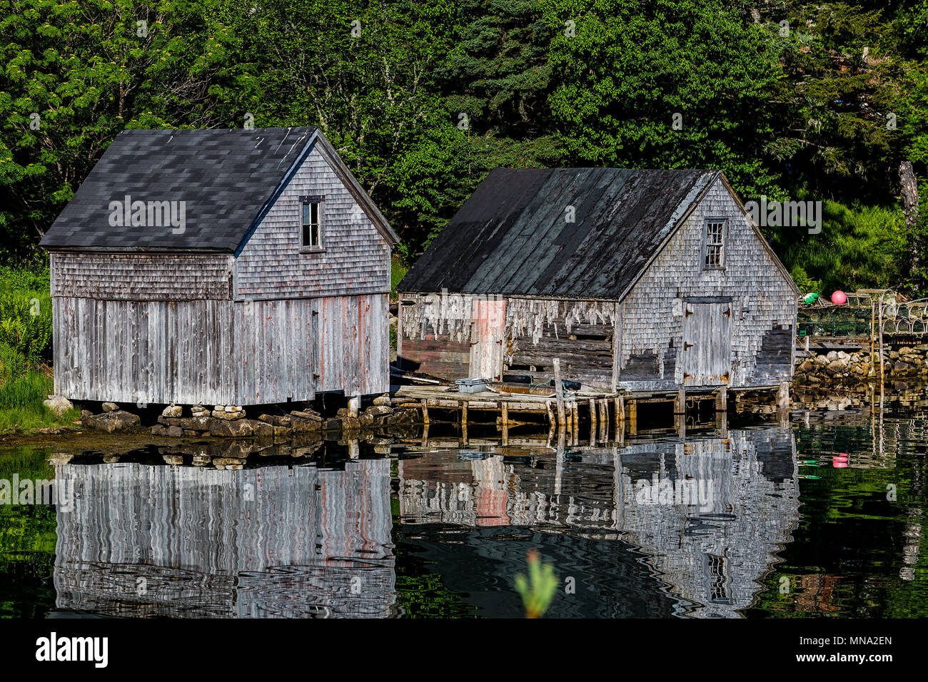 Vecchi capannoni di pesca che riflette ancora in acque lungo le rive della Nova Scotia, Canada. Foto Stock