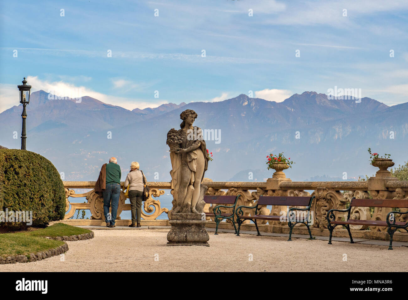 Una coppia di anziani gode di una vista mozzafiato sulle montagne e sul lago da una terrazza, sul Lago di Como, sulla Lombardia, sull'Italia Foto Stock