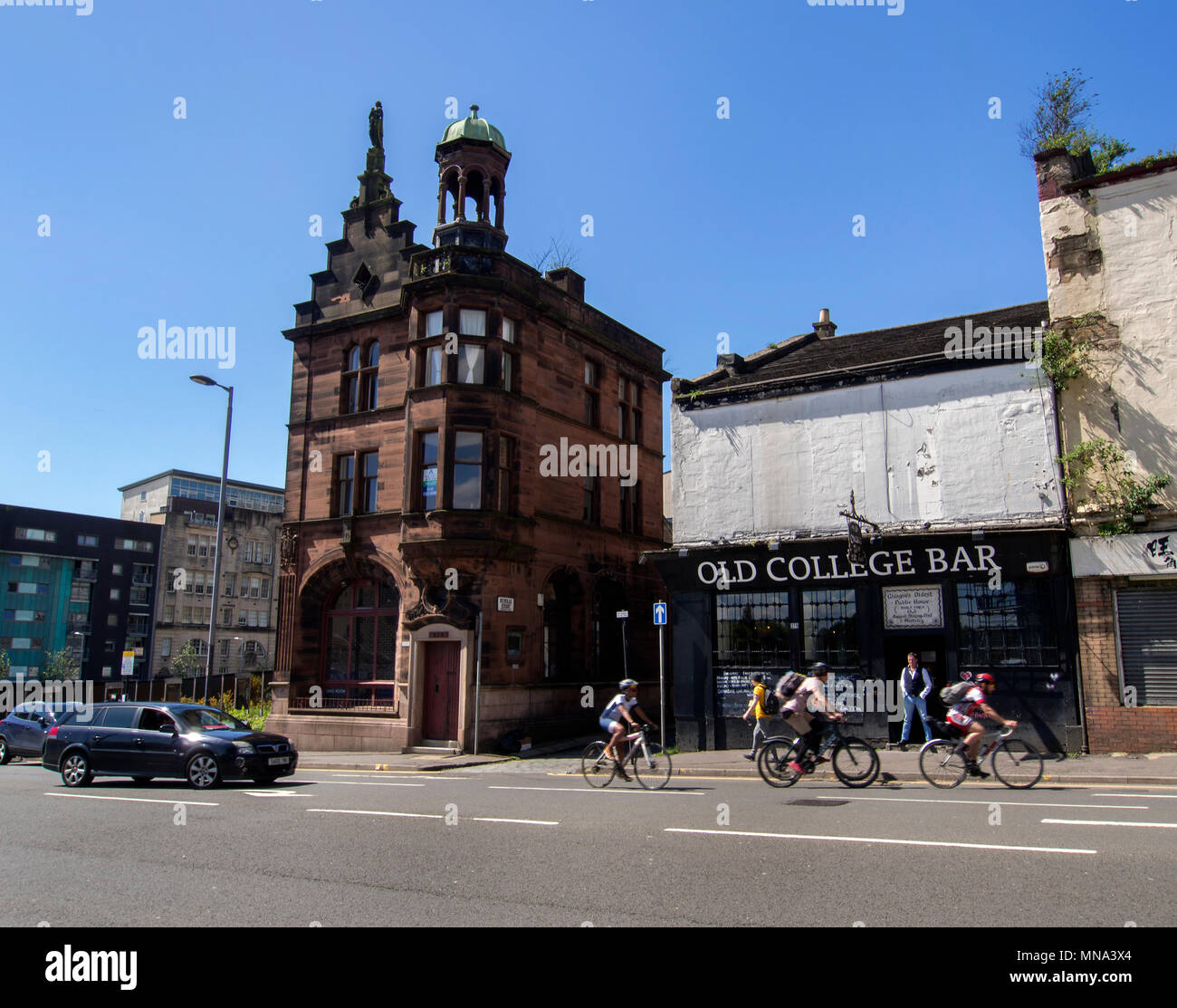 GLASGOW, SCOZIA - 13 Maggio 2018: i ciclisti e un pass auto del vecchio collegio Bar e la sala civica su High Street, Glasgow. Foto Stock