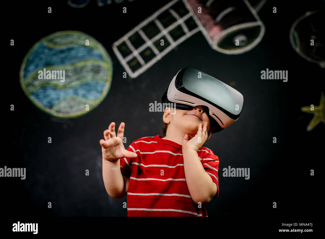 Ritratto di un giovane bambino indossando una realtà virtuale auricolare contro uno sfondo nero. Un ragazzino divertirsi con gli occhiali VR. Foto Stock