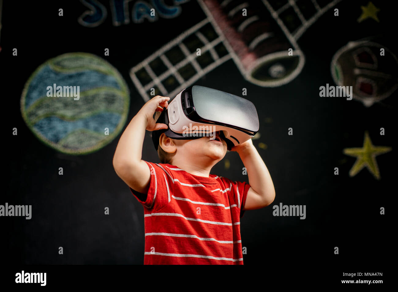 Ritratto di un giovane bambino imparare con una realtà virtuale auricolare su sfondo nero. Un ragazzino usando un occhiali VR. Foto Stock