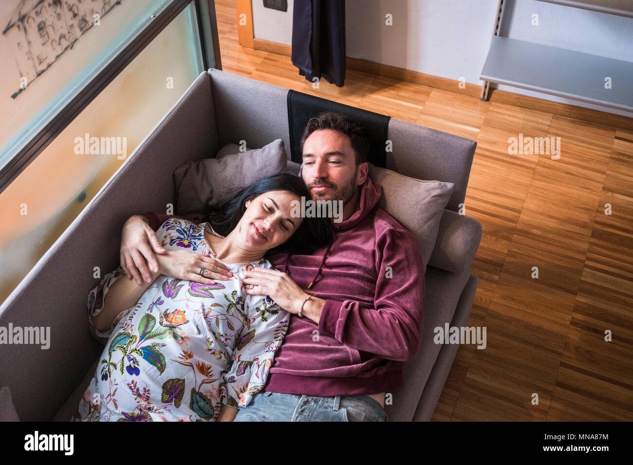 L uomo e la donna incinta riposare e stare sdraiati sul divano di casa. sorridente e dormire insieme in attesa per il nuovo bambino per rendere la famiglia completa. Foto Stock