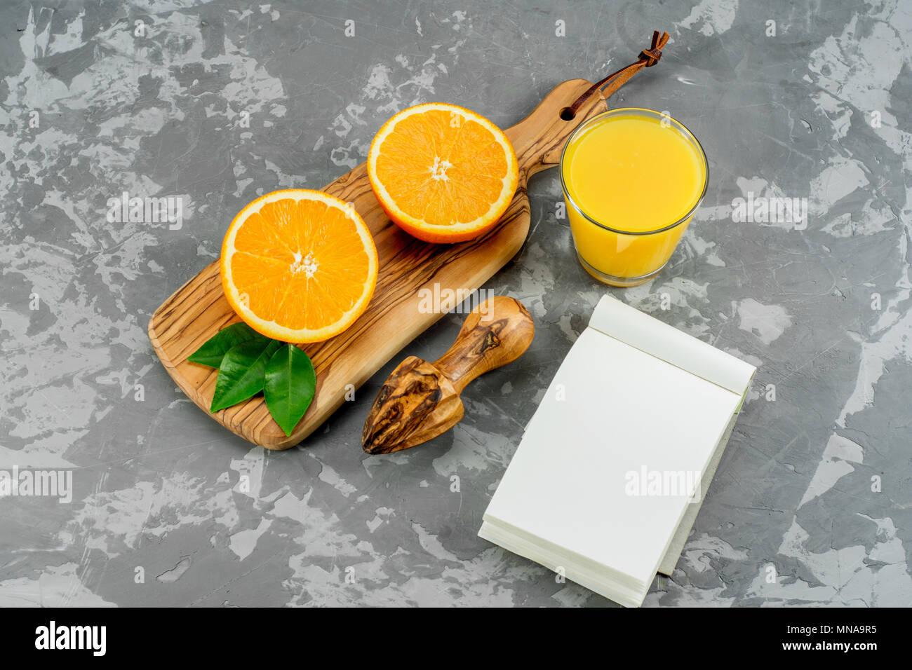 Ancora in vita un bicchiere di succo di arancia e fette di frutta arancione su sfondo di calcestruzzo con Notepad. Foto Stock