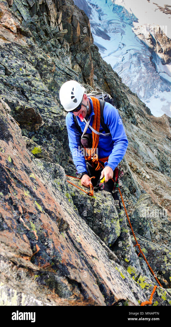 Maschio guida di montagna la costruzione di una tradizionale posizione di assicurazione con pitons rappel da un elevato picco alpino Foto Stock