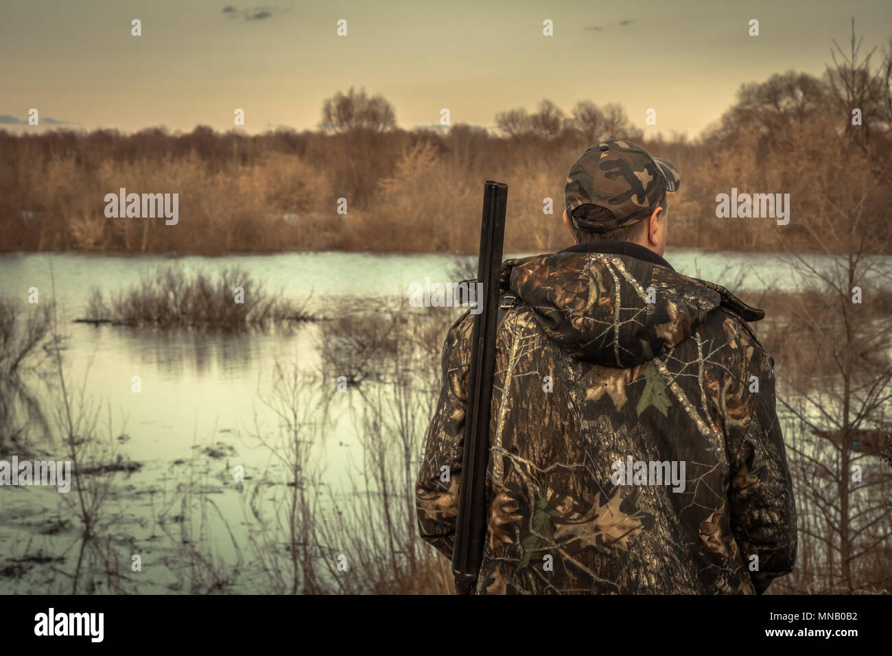 Hunter uomo fucile camouflage esplorare flood river stagione di caccia vista posteriore del tramonto Foto Stock