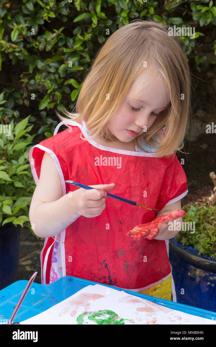 Due anni di pittura ragazza foto e disegni con vernici ad acquerello in giardino, ottenere vernice sulle mani. Abbigliamento protettivo. Foto Stock