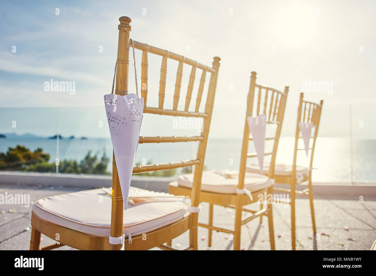 Spiaggia matrimoni setup con lo stile moderno dell'oro chiavari sedie con cono di petali di rose e di appendere la luce del tramonto direttamente dal lato righ Foto Stock