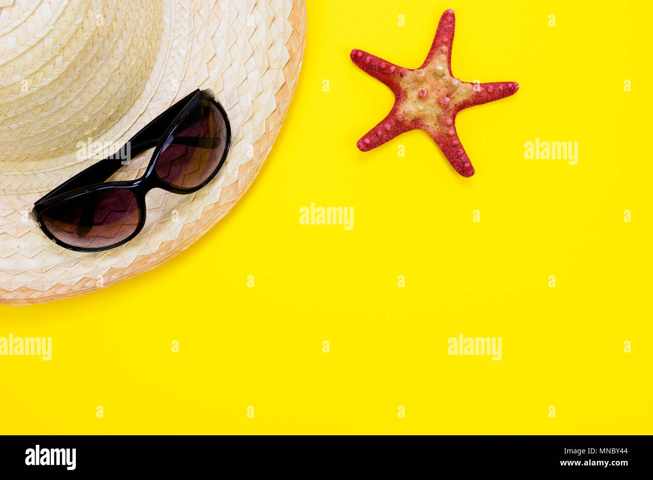 Vacanze estive e concetto di vacanza - Occhiali da sole, stella di mare e di una spiaggia retrò paglia su sfondo giallo con copia spazio. Foto Stock