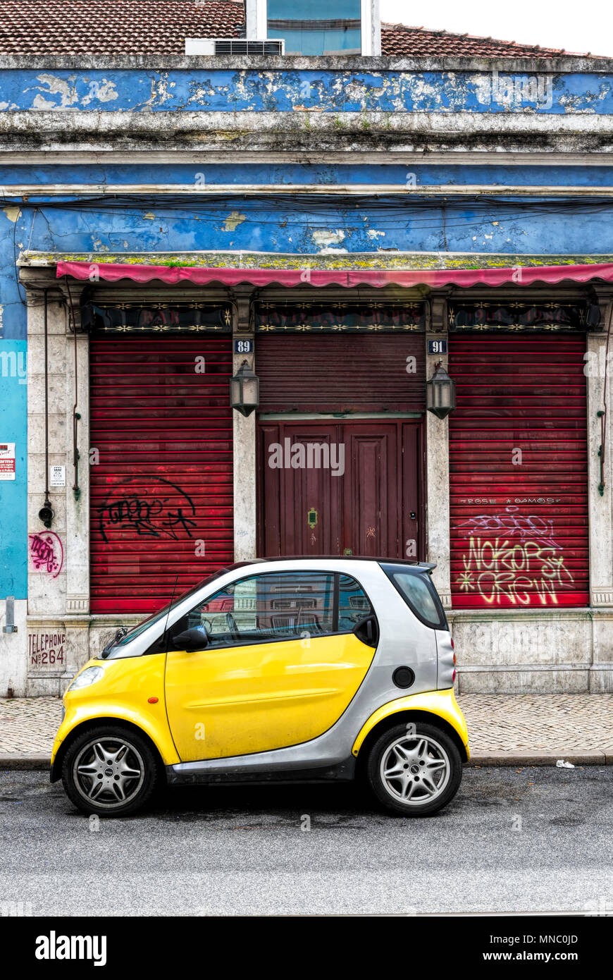 Luccicanti nuove giallo e argento smart fortwo auto parcheggiata di fronte fatiscente negozio chiuse Foto Stock