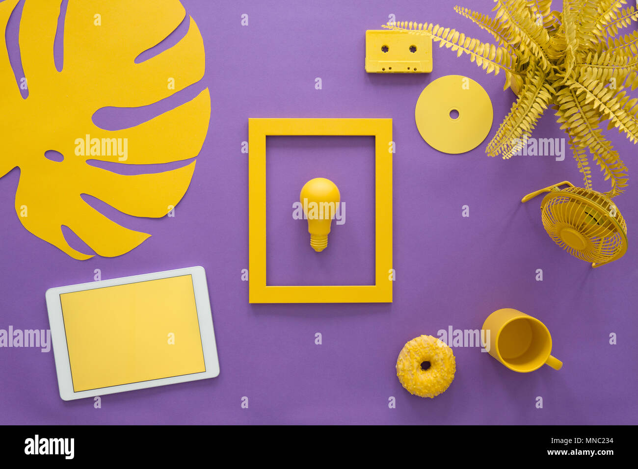 Vista dall'alto di una lampadina in un telaio, tablet, impianti e la ventola su uno sfondo viola di una scrivania creative Foto Stock