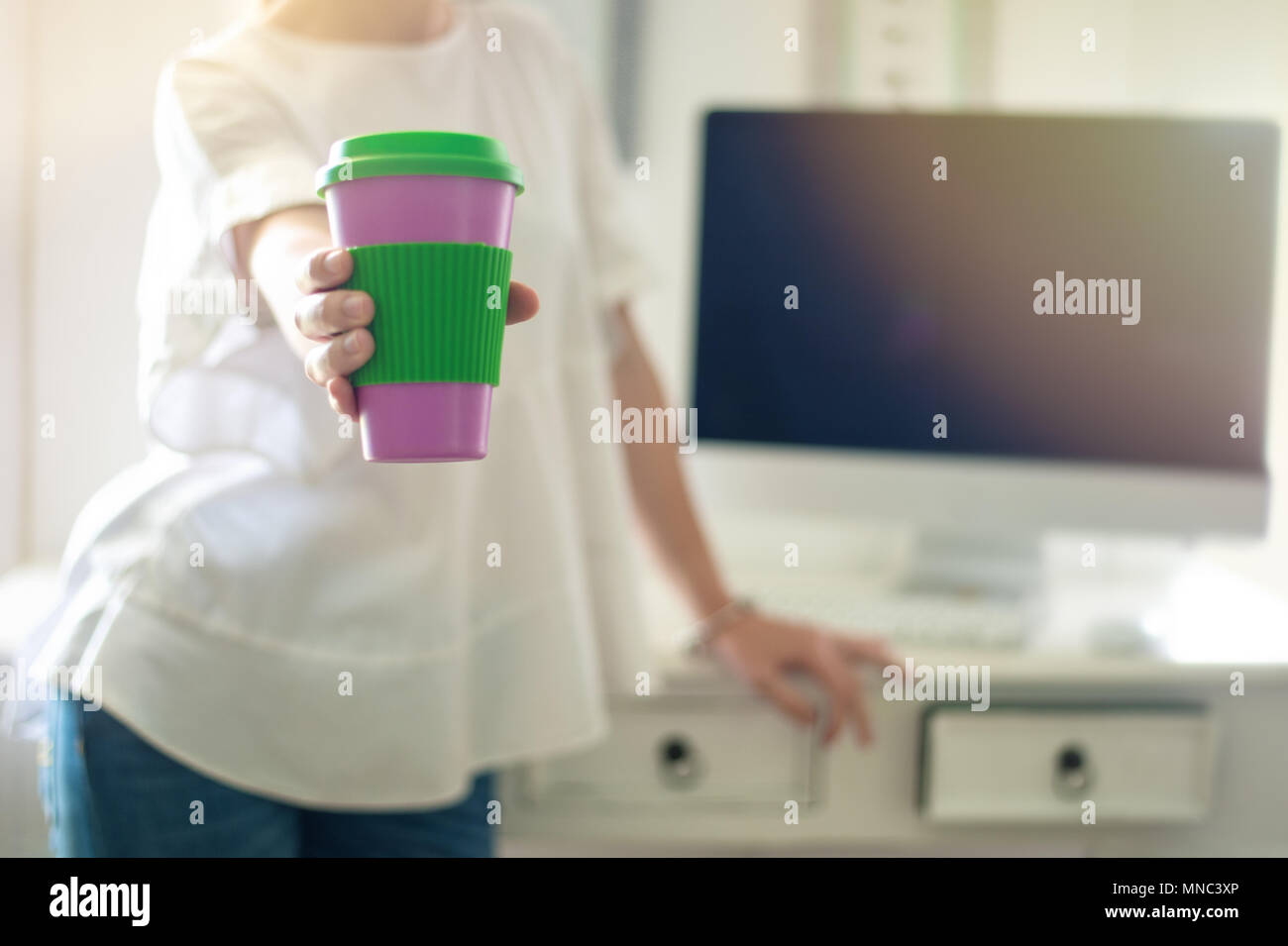 Chiudere fino al caffè per andare coppa in mano femminile che mostra alla telecamera, bianco interno di uno spazio di lavoro Foto Stock