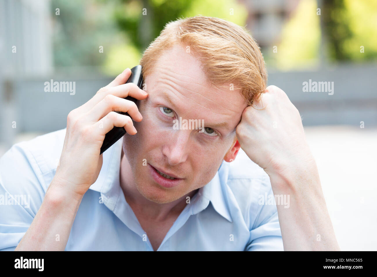 Closeup Ritratto, giovane arrabbiato, frustrato incazzato da qualcuno a parlare sul suo telefono cellulare, cattive notizie, isolata all'esterno al di fuori dello sfondo. Lo Foto Stock