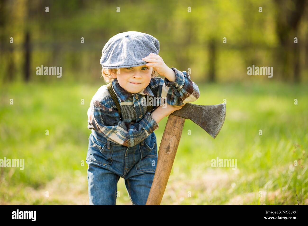Piccolo Ragazzo caucasico in hat in posa con grande ax. Ritratto di piccole lumberjack Foto Stock