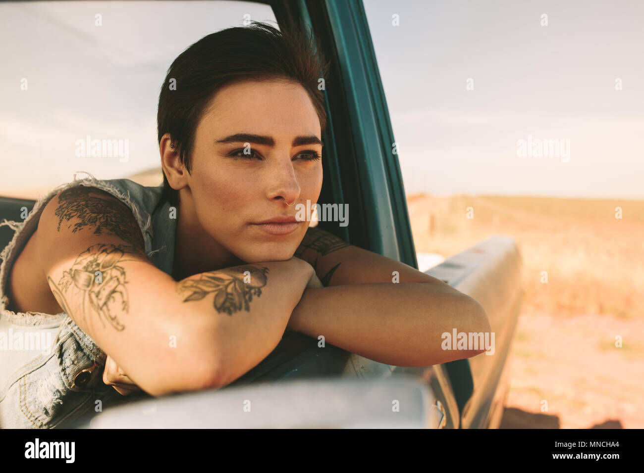 La donna su un viaggio in auto. Donna con tatuaggi su bracci guardando fuori della sua automobile seduto alla finestra. Foto Stock