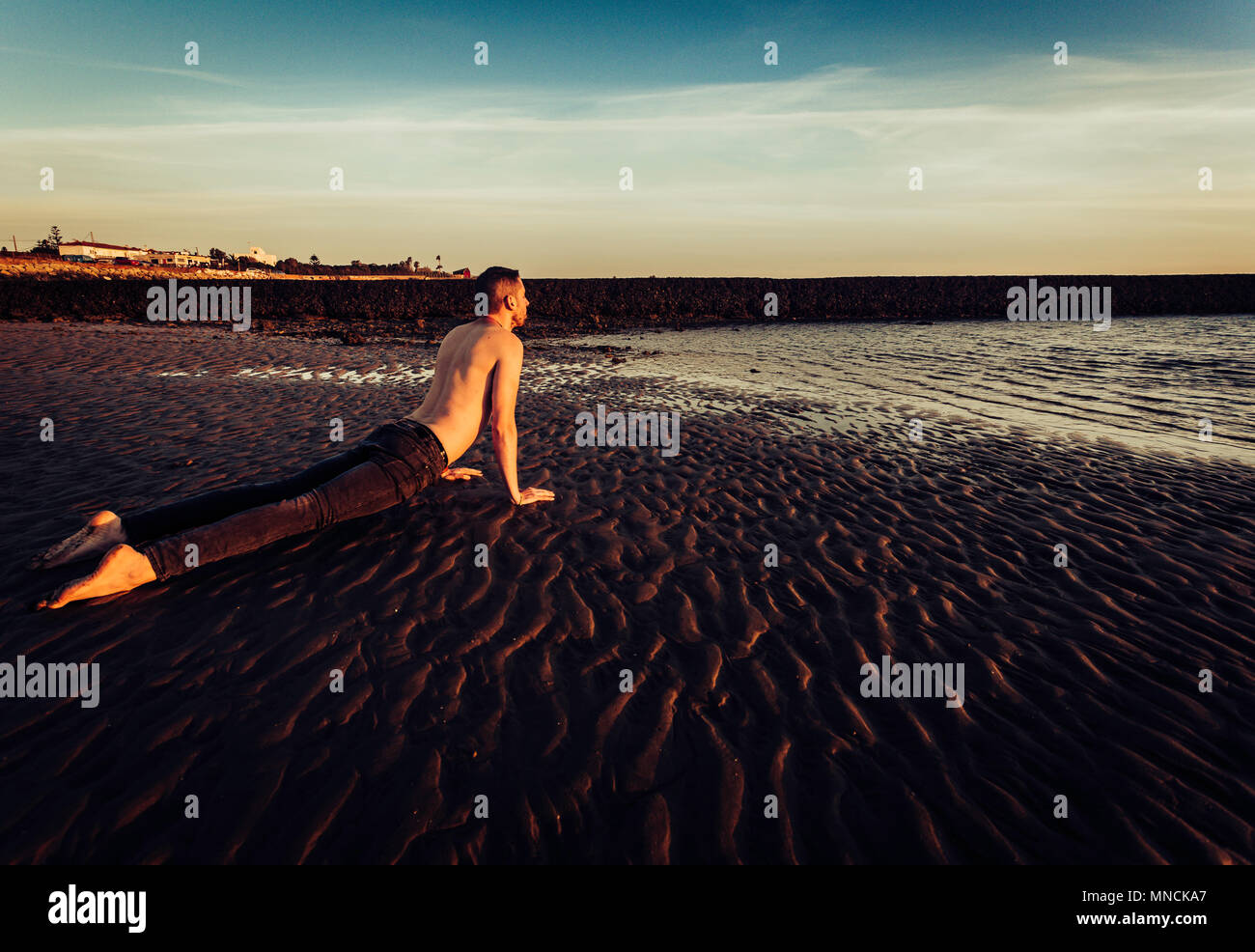Giovane uomo fare yoga sulla spiaggia di sabbia di Sanlucar de Barrameda quando la marea è bassa Foto Stock