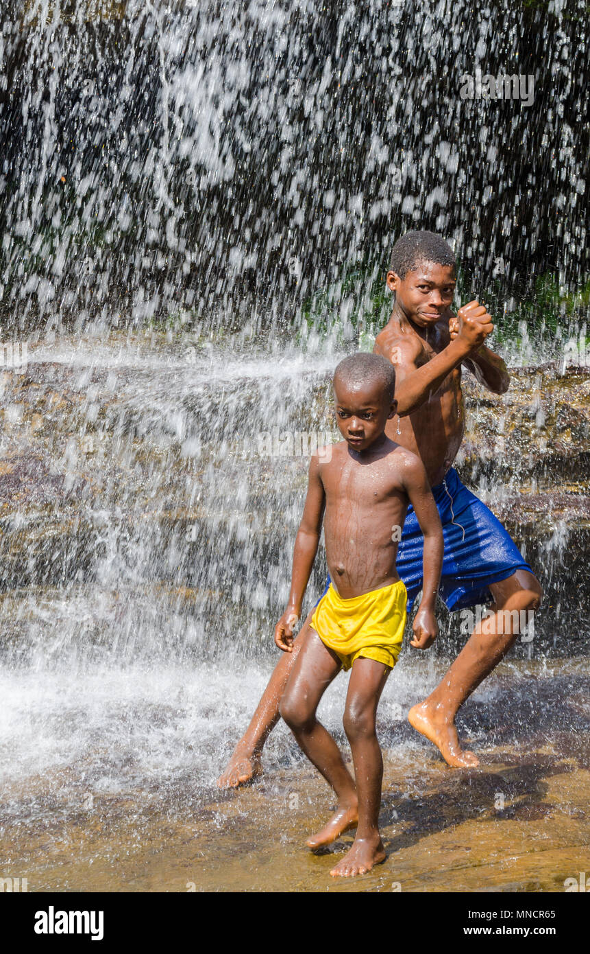 Kindia, Guinea - Dicembre 28, 2013: non identificato due giovani ragazzi africani wplaying e divertirsi sotto la cascata Foto Stock
