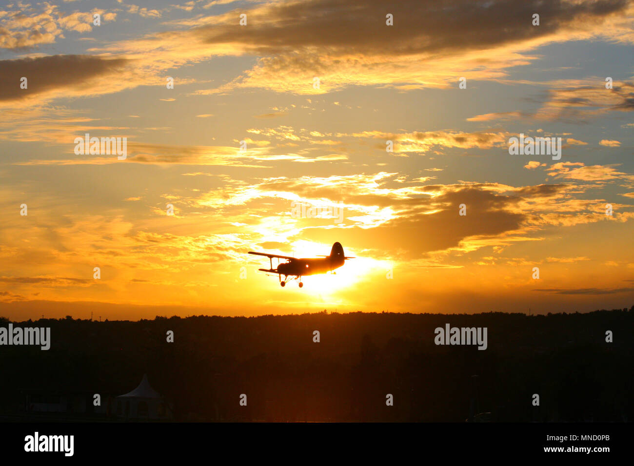 Un biplano volare sopra il cielo mentre il sole che tramonta dietro di esso. Ensoleillement momento. Foto Stock