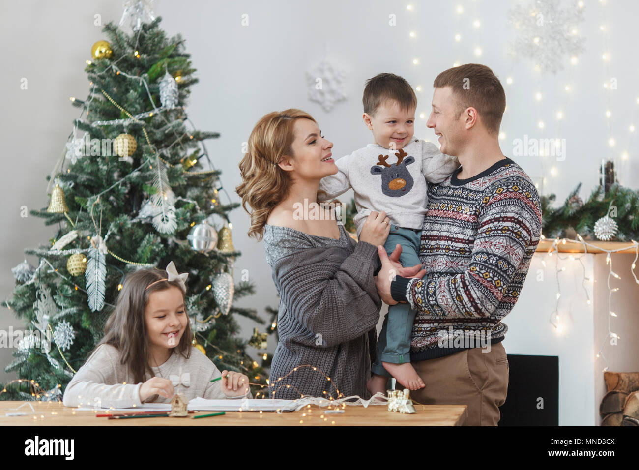 Il padre e la madre figlio di contenimento dalla figlia seduta a tavola contro l albero di Natale Foto Stock