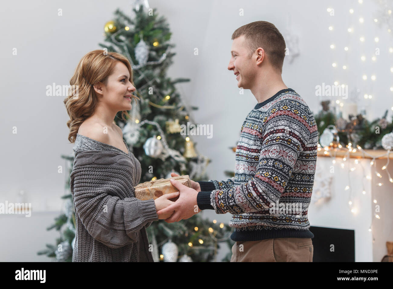 Vista laterale della coppia felice in piedi con la presente da albero di Natale a casa Foto Stock