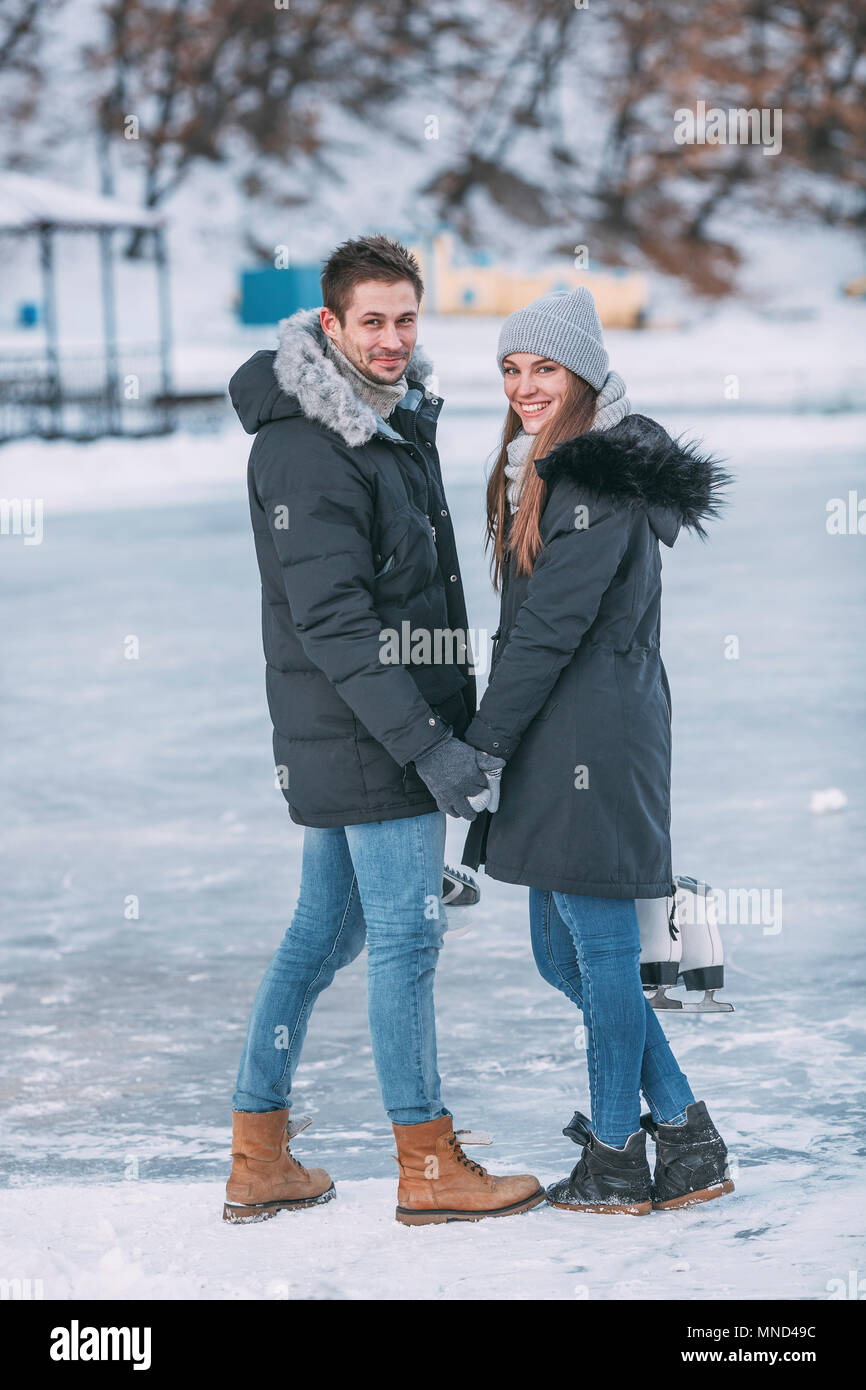 Per tutta la lunghezza della coppia felice guardando sopra la spalla mentre permanente sulla pista di pattinaggio su ghiaccio Foto Stock
