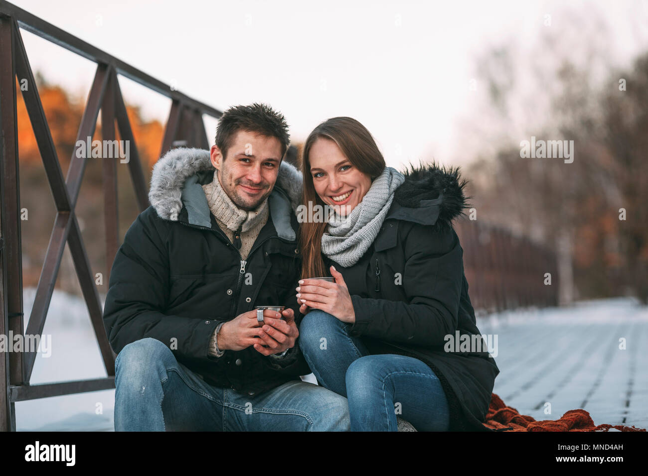 Ritratto di felice coppia seduta con bevande sul Boardwalk durante il periodo invernale Foto Stock