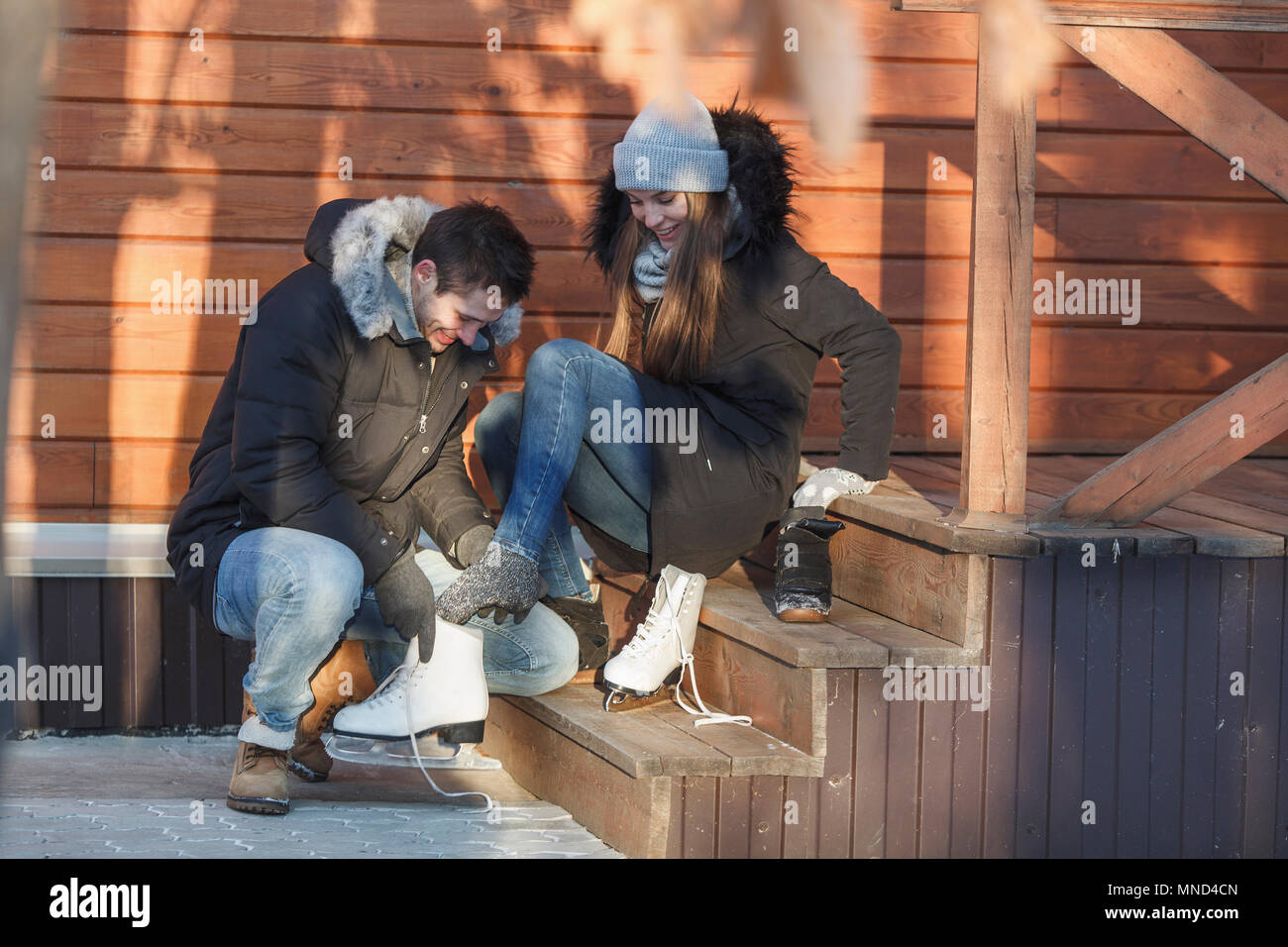 L'uomo accovacciato mentre assistono donna felice in indossando pattini da ghiaccio sulle fasi Foto Stock