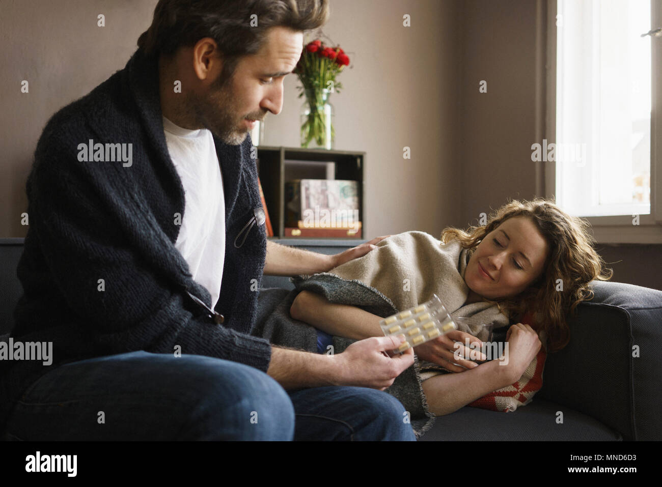 L uomo dando una pillola per ill donna sdraiata sul divano nel soggiorno di casa Foto Stock