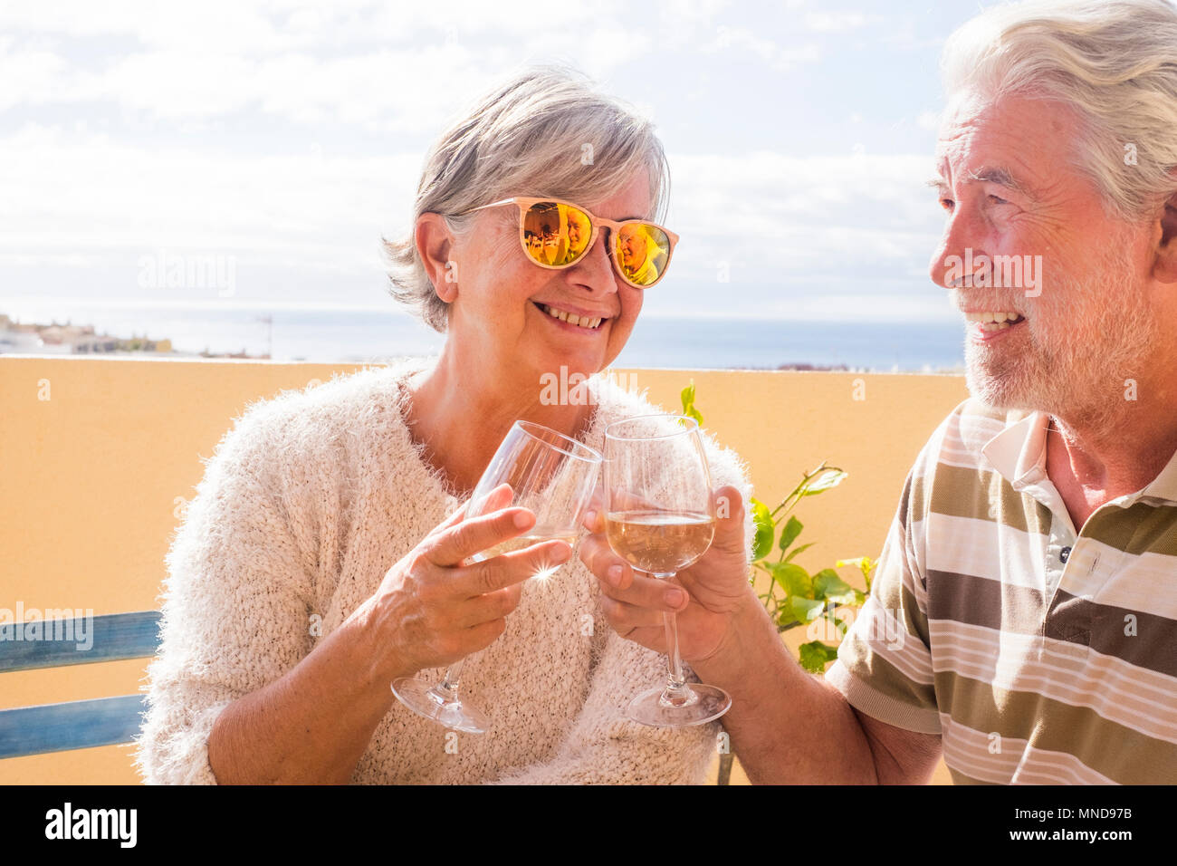 Coppia di anziani la tostatura con il vino in una terrazza esterna che si affaccia sul mare in estate Foto Stock