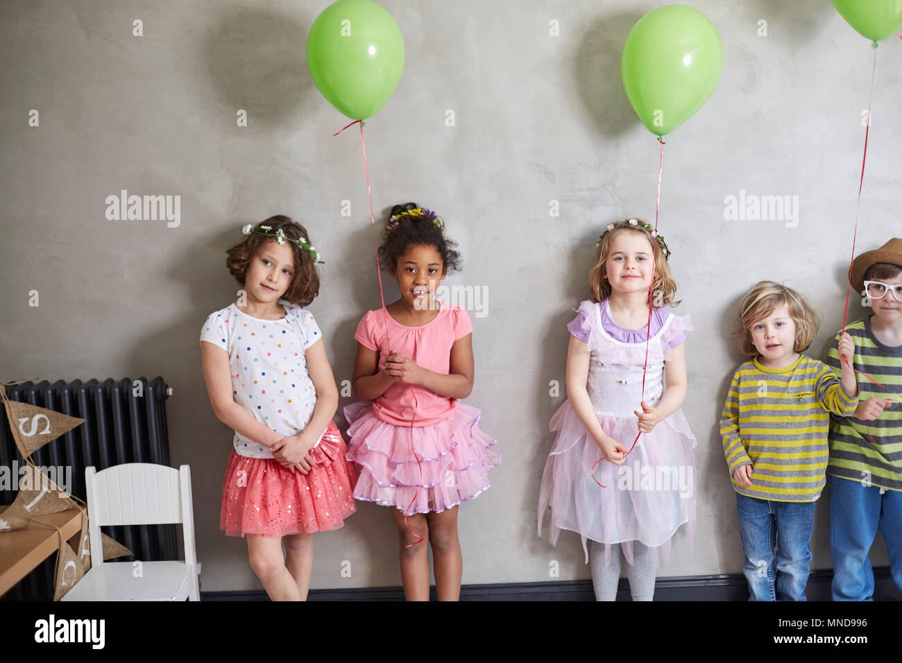 Ritratto di ragazze e ragazzi con palloncini verde in piedi contro la parete Foto Stock