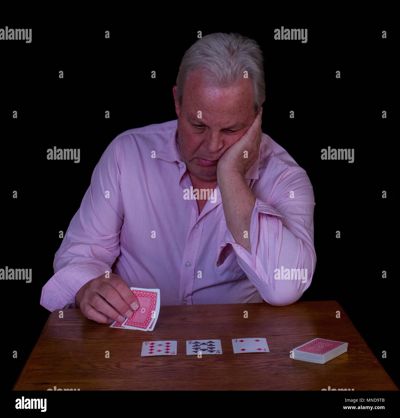 Uomo anziano con i capelli grigi cercando infelicemente presso la sua mano di poker immagine con spazio copia contro uno sfondo nero Foto Stock