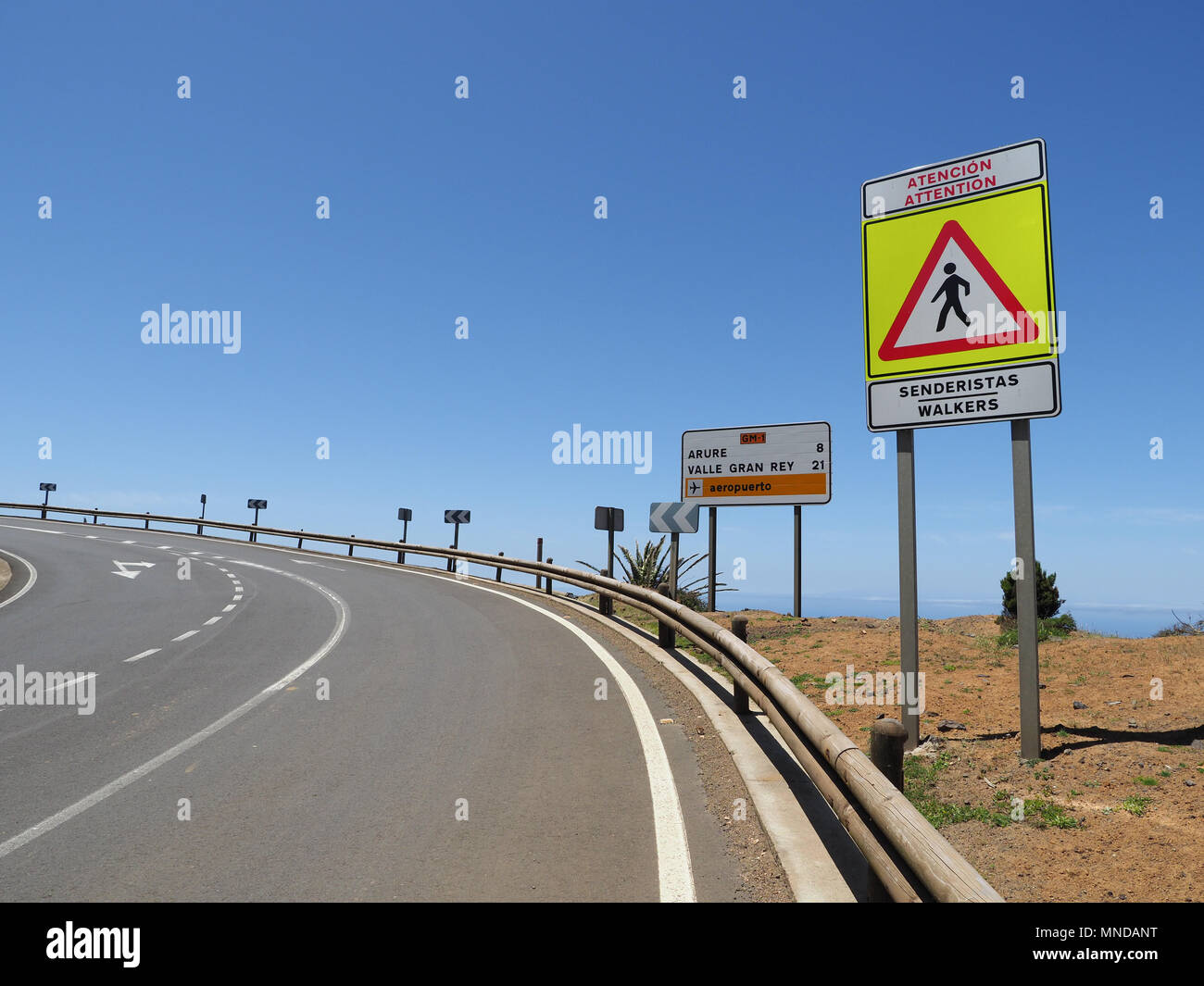 Il sentiero su una curva di una grande strada costiera a nord di La Gomera Canarie con chiara pedonale segno di avvertimento Foto Stock