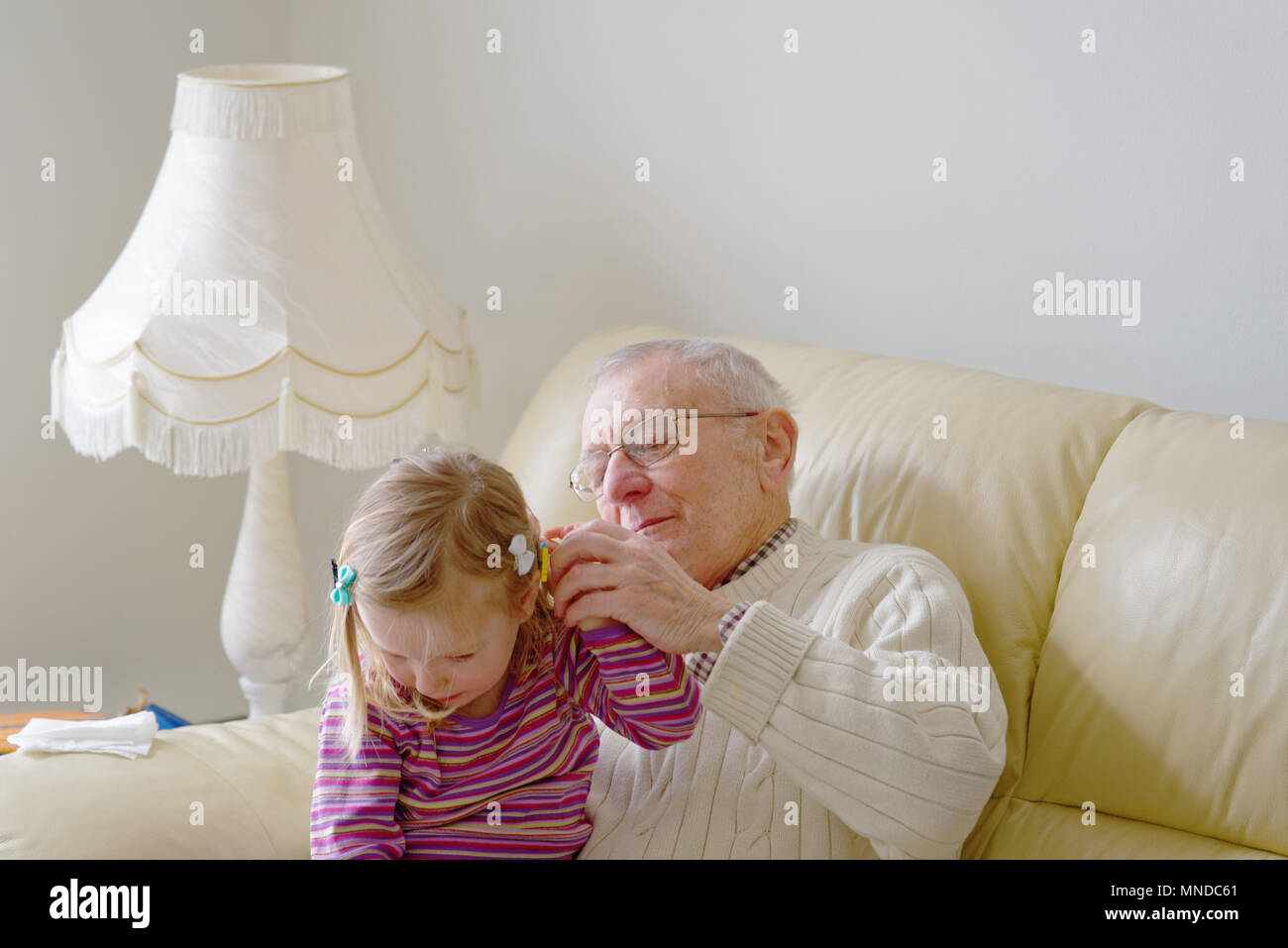 Un nonno regolando il fermacapelli della sua compagnia anno vecchio grand-figlia Foto Stock