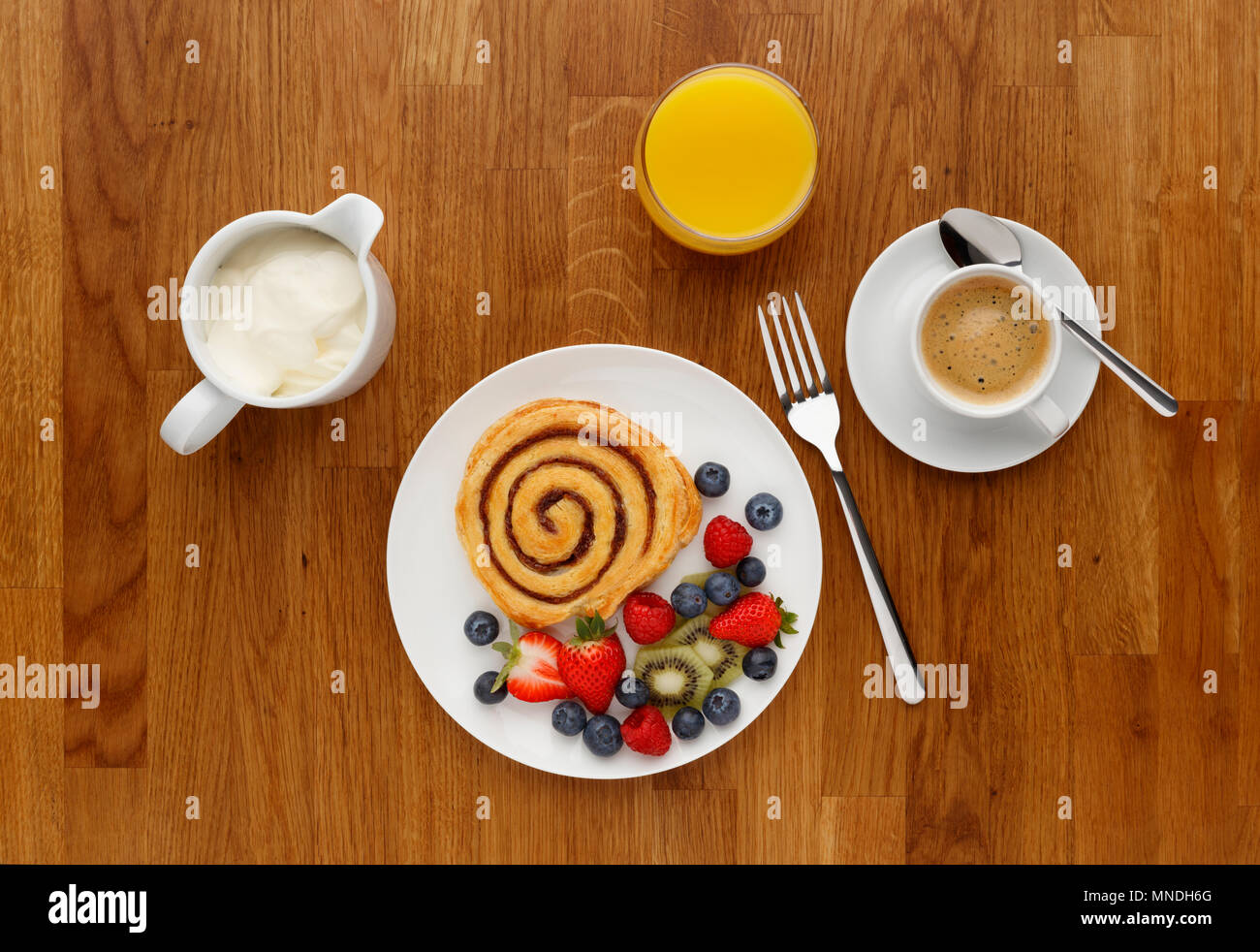 Un vortice di cannella prima colazione con frutta, caffè e succo d'arancia, girato su un sfondo di legno dal di sopra. Foto Stock