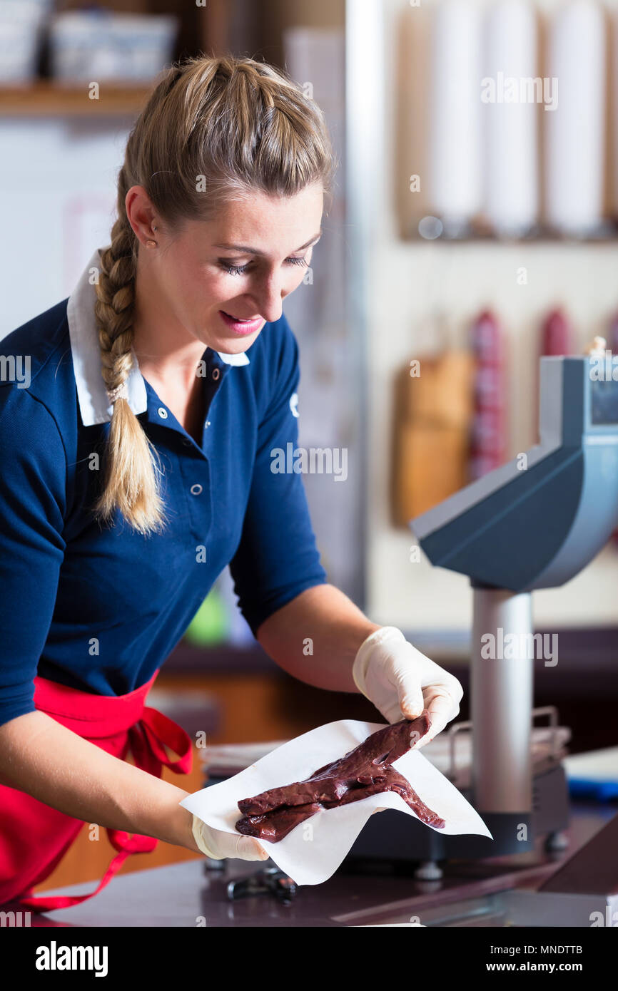 Donna di vendite nel negozio di macellaio mettere diversi tipi di carne nel display Foto Stock