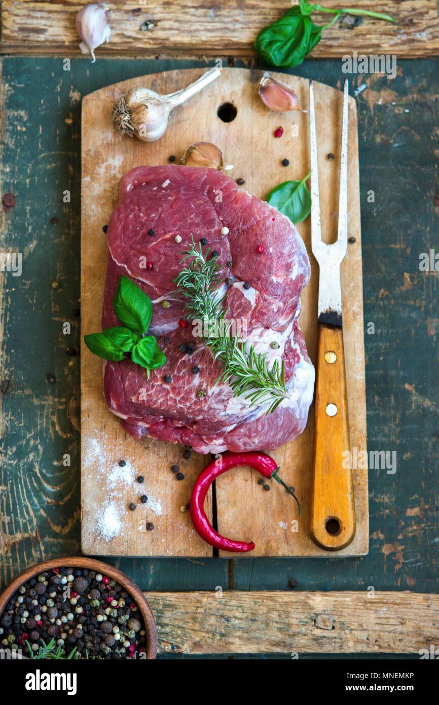 Carne di maiale cruda con erbe aromatiche, aglio, pepe e peperoncino su un tagliere Foto Stock