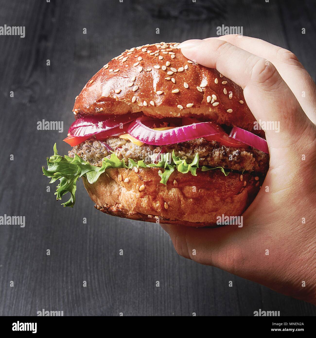 Una mano che tiene una fatta in casa beefburger con cipolla rossa Foto Stock