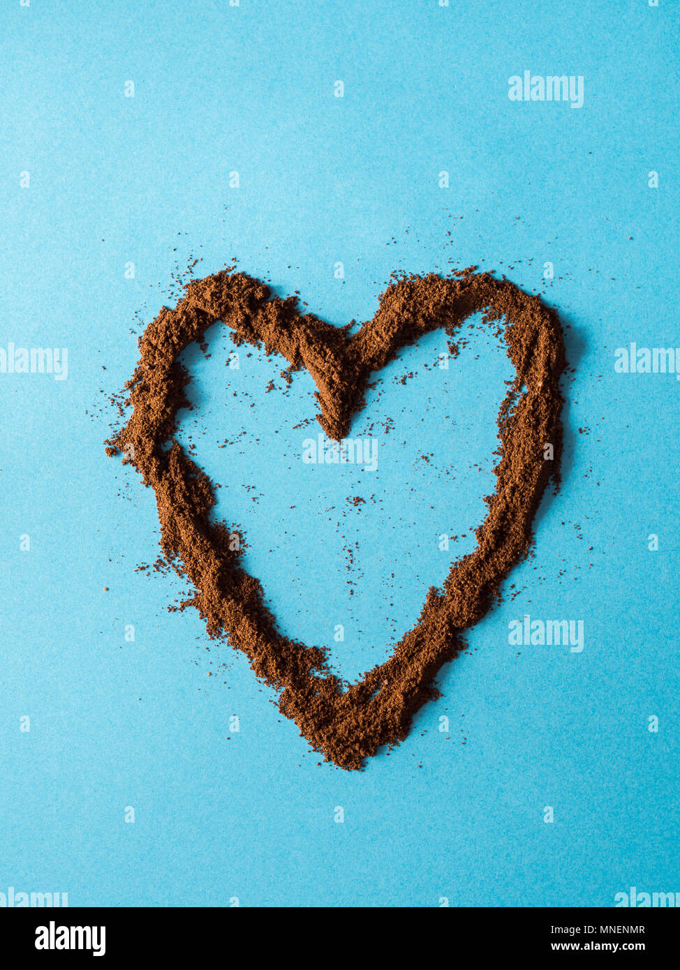 Cuore realizzato con caffè macinato in polvere su sfondo blu Foto Stock