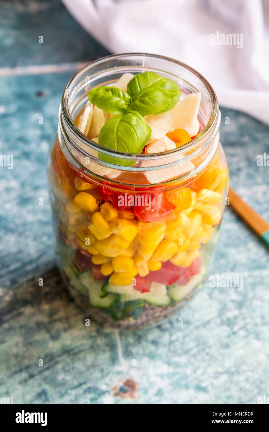 Una variopinta insalata in un vasetto di vetro con il rosso la quinoa, cetrioli, peperoni, mais, pomodori, pecorino e basilico Foto Stock